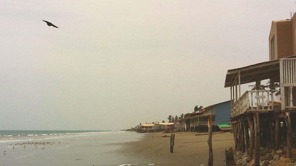 Balneario del norte peruano fuera de temporada: fila de casas de playa cerradas bajo cielo gris, sin gente en la arena.