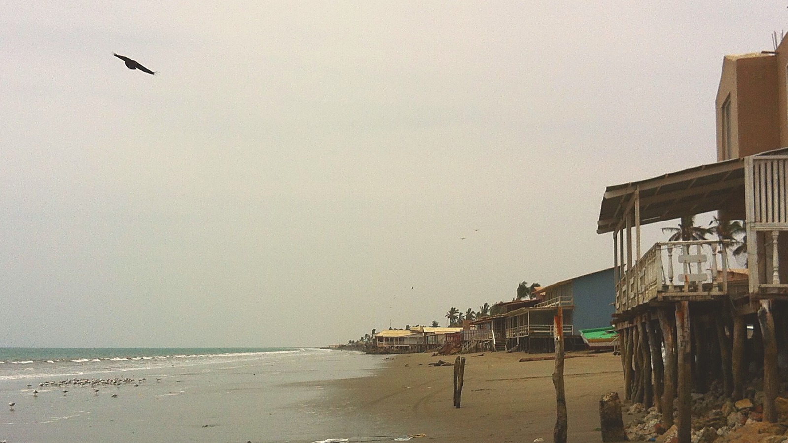 Balneario del norte peruano fuera de temporada: fila de casas de playa cerradas bajo cielo gris, sin gente en la arena.